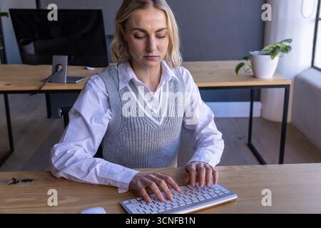Female office worker typing on wireless keyboard at office desk with monitor Stock Photo