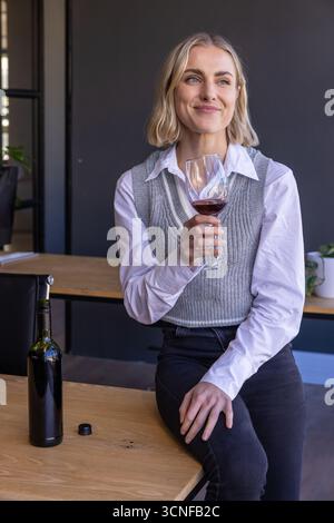 Female drinking red wine beside wine bottle on table in modern tasting room Stock Photo