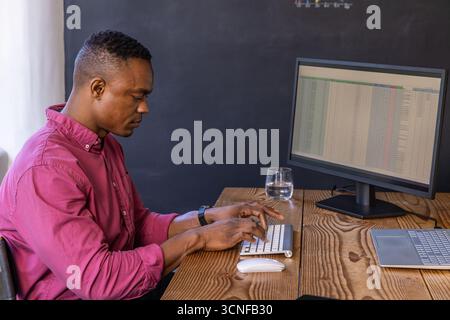 African american man typing spreadsheet data on wireless keyboard at desk in home office Stock Photo