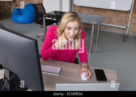 Woman working on laptop and monitor at coworking office desk using wireless mouse and keyboard Stock Photo