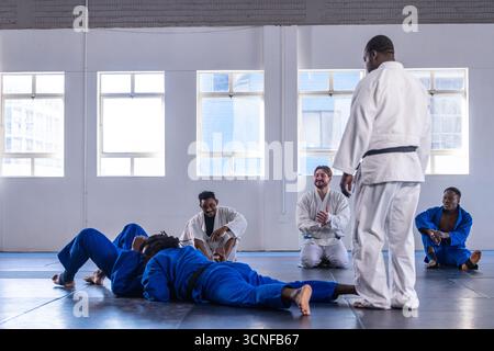 Diverse martial class with instructor practicing sparring in gis on mats in studio, copy space Stock Photo