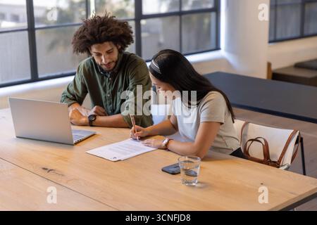 Male middle eastern colleagues collaborating over laptop, document at table in meeting room Stock Photo