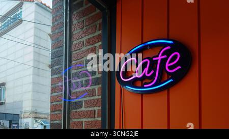 Glowing cafe neon sign on a vibrant orange wall reflecting in the window Stock Photo