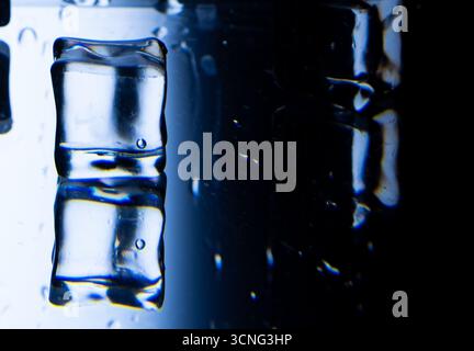 2.Rectangular ice cube on a wet, reflective surface. The transparent cube has trapped air bubbles and reflects blue and white light. Water droplets ar Stock Photo