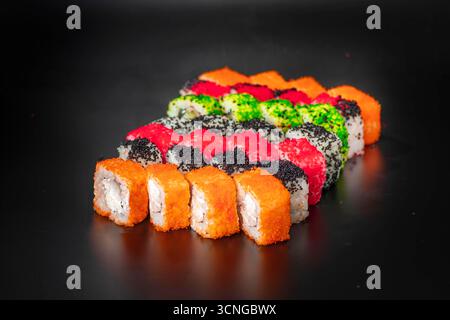 A colorful assortment of sushi rolls arranged neatly on a black surface. The rolls feature various toppings and fillings, showcasing vibrant colors an Stock Photo