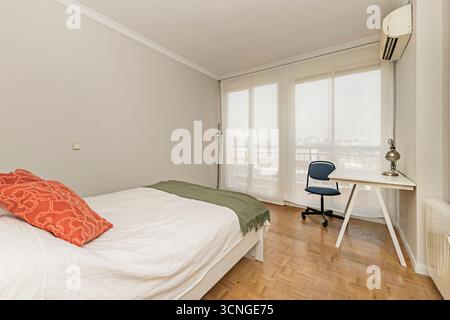 Modern bedroom with light wood bed, study table on casters, and adjustable stool Stock Photo