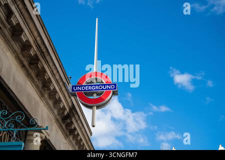 Close-up of the iconic London Underground red and blue roundel sign on a building facade, set against a clear blue sky. Stock Photo