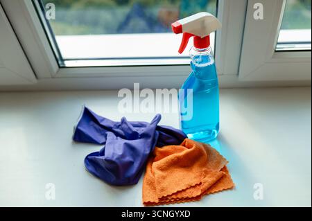 Cleaning spray, cloth and gloves placed on a windowsill, preparing for window washing and household chores Stock Photo
