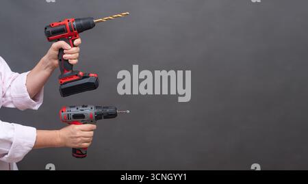Two cordless drills held in hands, red and black tools with drill bits extended, isolated background, repair and DIY projects. Pair of cordless drills Stock Photo