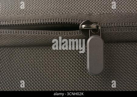 black half opened zipper with plastic rectangle pull tab on black textured fabric bag surface in close-up macro view, security and modern design Stock Photo