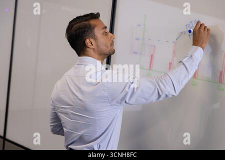 Man writing on whiteboard in office and annotating colored bar charts with blue marker Stock Photo