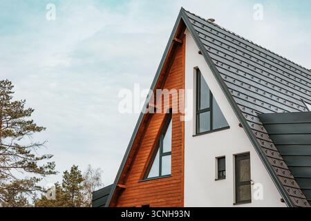 Gable roof of a contemporary A frame house with triangular windows and wood cladding Stock Photo