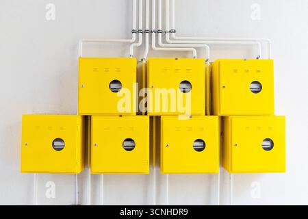 Row of yellow electric meters measuring electricity or water or gas consumption mounted on a white wall with visible pipes Stock Photo