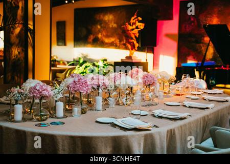 Luxurious table set for an elegant gathering featuring pink and white floral centerpieces, candles, and polished dinnerware in a sophisticated environ Stock Photo