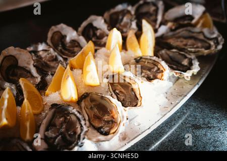 Fresh oysters served on ice with lemon wedges on a platter. The image captures the seafood's freshness, ready for dining, highlighting the contrast be Stock Photo