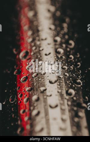 Water droplets on a reflective metallic surface with a red light. The focus is on the wet texture and reflections. Abstract composition in dar low key Stock Photo