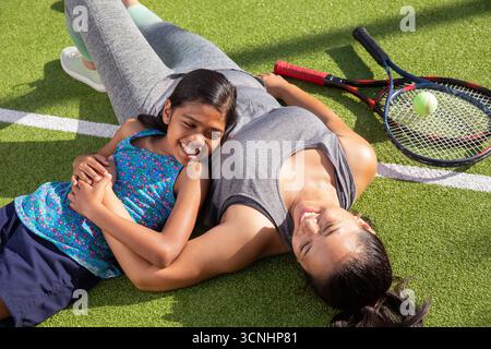 Asian sisters lying side by side wearing sportswear on tennis court near rackets and tennis ball Stock Photo