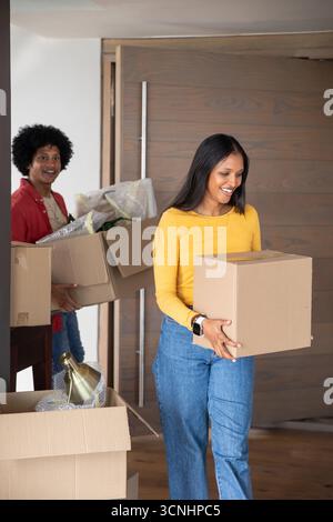 Diverse couple carrying cardboard boxes with bubble wrap and metallic lamp base into foyer Stock Photo