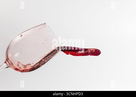 Tilted wine glass, spilling wine in a forward line, the background is white and the glass looks dirty Stock Photo