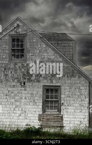 An old wooden house stands weathered and worn, surrounded by a dark, cloudy sky. The atmosphere feels eerie as the clouds loom overhead, enhancing the Stock Photo