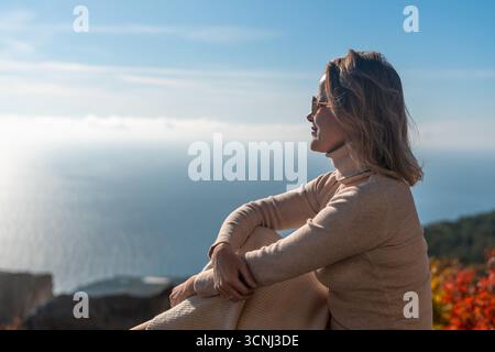 Woman Ocean View Contemplation: Mature woman sits peacefully overlooking a vast ocean on a sunny day, finding solace in nature's beauty. Stock Photo