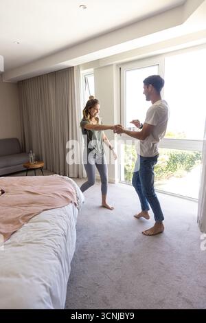 Couple holding hands and smiling in bright carpeted bedroom near sliding glass door Stock Photo