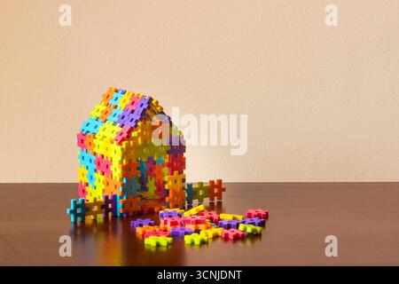 Colorful interlocking plastic bricks forming a house on a wooden table, symbolizing construction, playing, and real estate investment Stock Photo