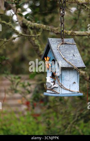 Quaint, blue decorative wooden birdhouse hangs from a tree in a garden in Carmel-by-the-Sea, CA. Stock Photo