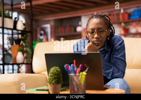 Independent woman using laptop for remote job tasks at home office, doing research and enjoying the benefits of schedule flexibility. Embracing the modern lifestyle of freelance work. Stock Photo