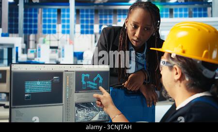 Photovoltaics factory manager supervising work done by specialist building models of renewable energy generators. Solar panels plant supervisor overseeing technician building solar cells, camera A Stock Photo