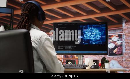Admin doing maintenance on artificial intelligence neural networks computerized model, listening music. Tech support specialist wearing headphones doing checkup on AI systems, camera A Stock Photo