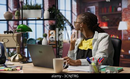 Remote employee pausing work done on laptop at home to pensive thinking. Teleworker in apartment feeling bored by repetitive tasks, stopping work on notebook to daydream, camera B Stock Photo