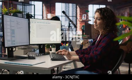 Smiling woman using programming languages on PC in IT startup office to build applications. Upbeat programmer using computer in software development agency to code, camera A Stock Photo