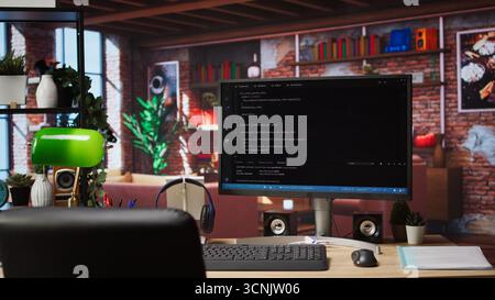 Coding interface shown on computer screen on desk in bright home office. Command lines written in code editor program UI on PC display in modern cozy home living room workspace Stock Photo
