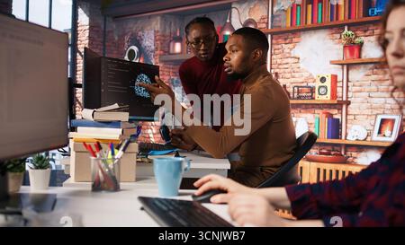 Team of startup workers conducting code review on PC to fix bugs, identifying technical issues with artificial intelligence company software. IT staff members optimizing code using device, camera A Stock Photo