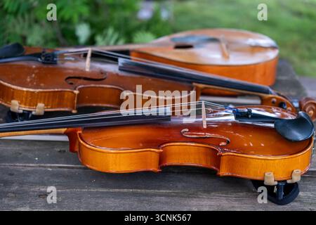 Three beautifully crafted wooden violins are placed on a rustic table, highlighting their rich colors and textures, set against a lush green backgroun Stock Photo