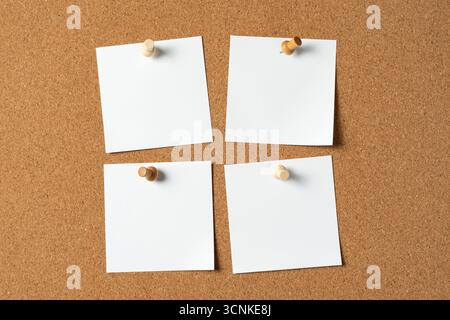 Four blank white notes pinned to a cork bulletin board with wooden push pins, creating space for reminders, messages, or ideas in an organized layout. Stock Photo