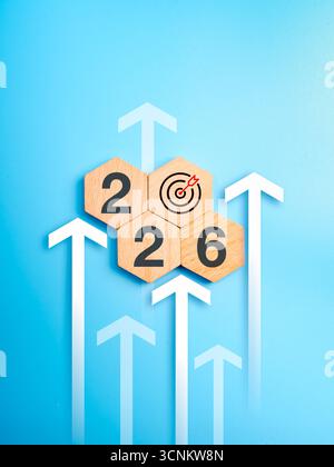 Wooden hexagon blocks showing 2026 and target icon with upward arrows on blue background, representing new year business growth, planning for success, Stock Photo