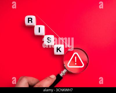 Weak cybersecurity and online scam concept with cubes down steps with RISK text and magnifying glass focus on warning symbol on red background. Fraud, Stock Photo
