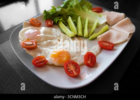Close up of healthy breakfast with fried eggs, fresh cucumber, lettuce, cherry tomatoes and turkey slices served on white plate. Concept of healthy ea Stock Photo