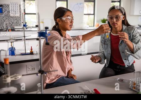 Two female students in lab wearing safety goggles and examining test tube rack Stock Photo