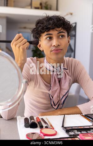 Man applying facial makeup at apartment table using brush, mirror and eyeshadow palette Stock Photo
