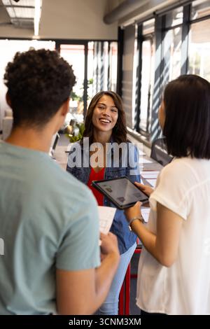 Diverse coworkers collaborating around printed documents and using tablet at office desk Stock Photo
