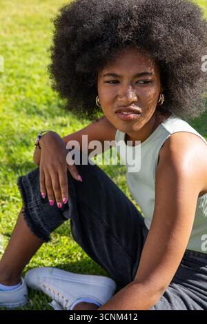 African american woman sitting on park lawn looking aside wearing gold hoop earrings Stock Photo