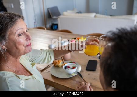 Senior woman and man sharing breakfast at dining table with orange juice glasses Stock Photo