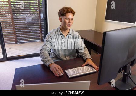 Man working at desk on computer while typing on keyboard, using mouse in home office Stock Photo