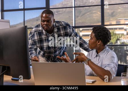 African american colleagues leaning over desk toward laptop and desktop monitor in office Stock Photo