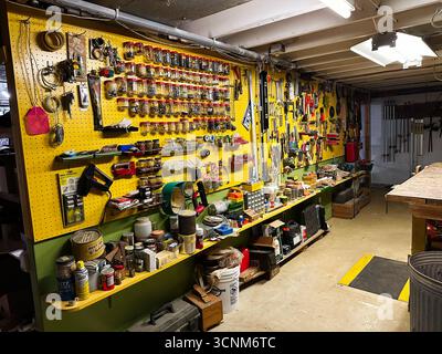 Jenkintown, Pennsylvania, USA - April 25, 2025: A busy workshop setup with a yellow pegboard wall, shelves, and hanging tools in a bright workspace. Stock Photo
