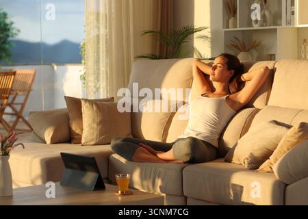 Yogi relaxing after yoga exercises sitting on a couch at sunset at home Stock Photo