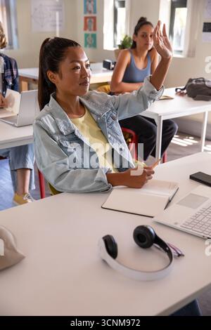 Female students raising hand, writing in notebook with pencil and typing on laptop Stock Photo